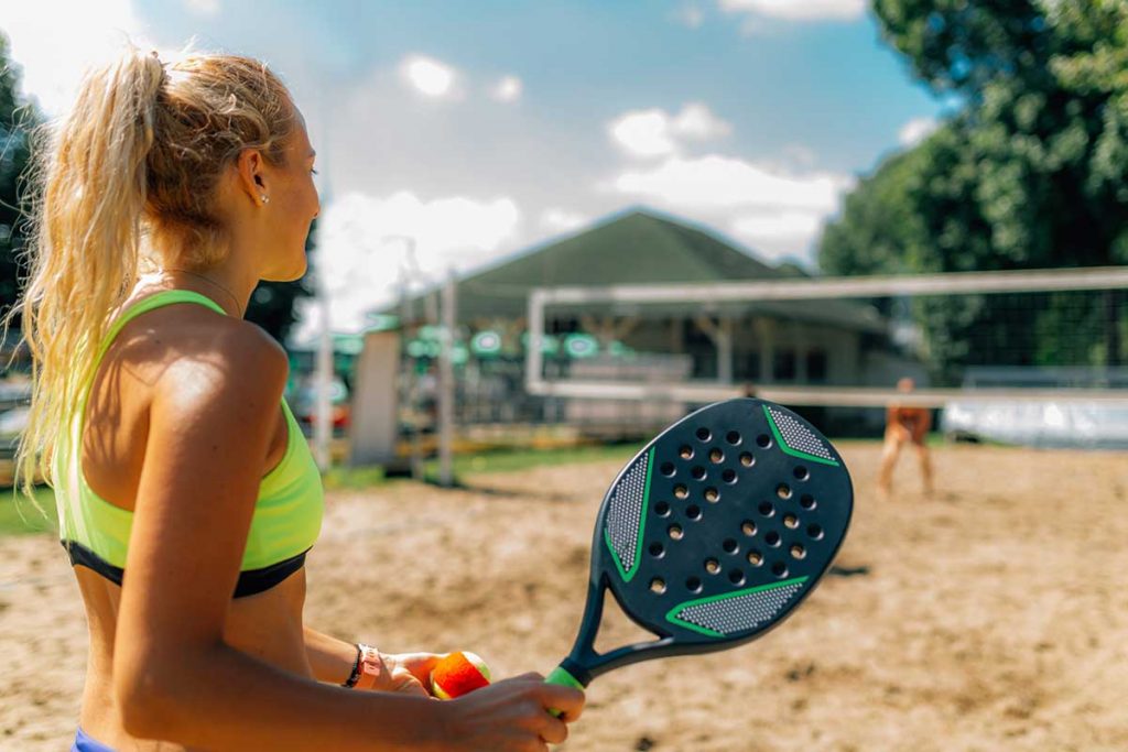 Mulher jogando beach tennis na quadra de areia. Dicas para praticar beach tennis como treino muscular e aeróbico